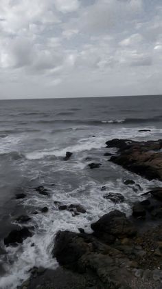 an ocean view with rocks and water in the foreground, under a cloudy sky