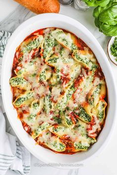 a white dish filled with spinach and cheese on top of a table next to carrots