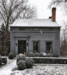 the house is covered in snow and has hedges on both sides with bushes around it