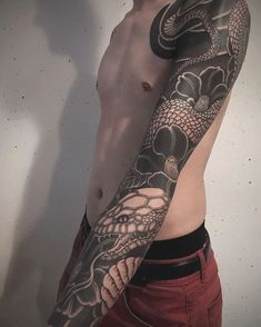 a man with a dragon tattoo on his arm and chest is standing in front of a wall