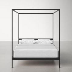 an iron bed frame with white sheets and pillows on the bottom, in front of a gray wall