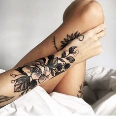 a woman laying on top of a bed with her legs crossed and tattoos on her arm