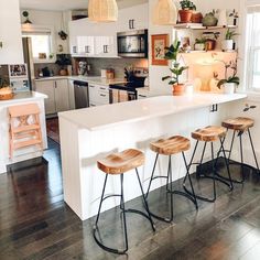 a kitchen with three stools in front of an island and several potted plants on the counter