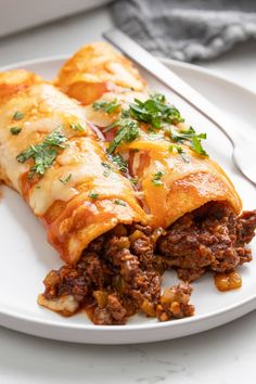 two enchiladas are sitting on a white plate with a fork and knife