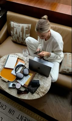 a woman sitting on a couch looking at her cell phone and laptop computer with headphones