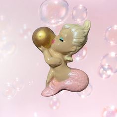 a little mermaid figurine sitting on top of bubbles in front of a pink background