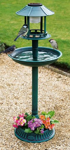 a bird feeder with two birds on it and flowers in the bottom right hand corner