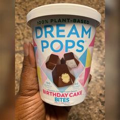 a hand holding up a cup of ice cream with chocolate toppings on top and the words dream pops written in it