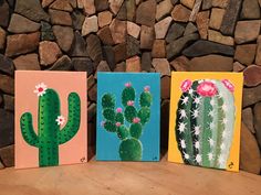 three small paintings of cactuses on canvases sitting on a wooden table in front of a stone wall