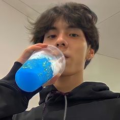 a young man is drinking from a blue water bottle while wearing a black hoodie