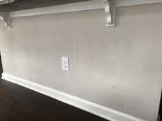 an empty room with a light switch on the wall and wood floors in front of it