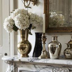 three vases filled with white flowers sitting on top of a marble table next to a mirror