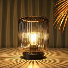 a glass lamp sitting on top of a wooden table next to a palm tree branch