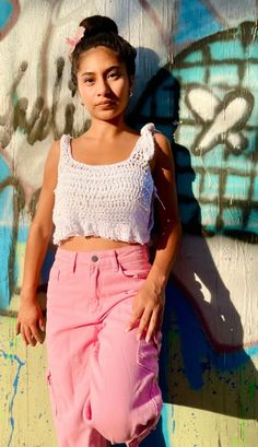 a woman standing in front of a wall with graffiti on it and wearing pink pants