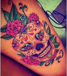 a woman's thigh with a colorful sugar skull and flowers tattoo on her leg