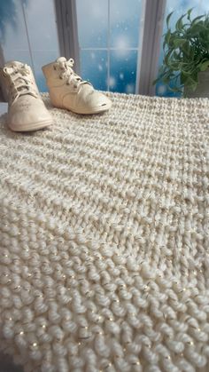 two pairs of shoes sitting on top of a white knitted tablecloth next to a potted plant