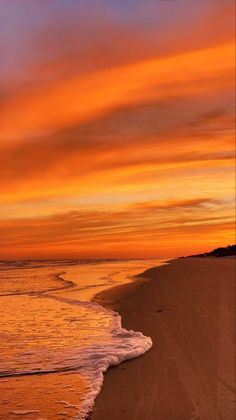 an orange and blue sunset over the ocean with waves coming in to shore on a sandy beach