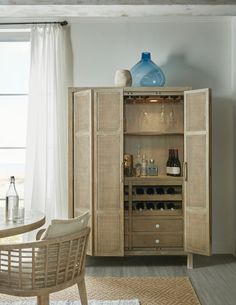 a wooden cabinet with bottles and glasses on it in a room next to a window