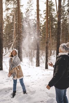 two people standing in the snow near trees and sprinkleing snow on them