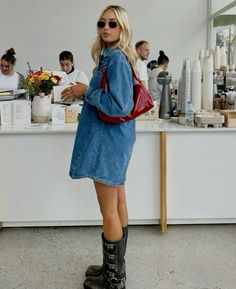 a woman standing in front of a counter holding a red purse and looking at her cell phone