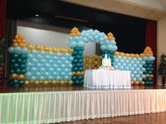 a table topped with a cake covered in blue and gold balloons on top of a wooden floor