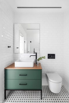 a bathroom with black and white flooring and green cabinetry, along with a toilet