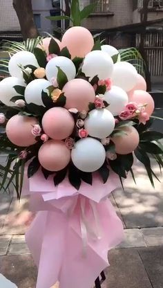 a bouquet of pink and white balloons with greenery in the center on a sidewalk