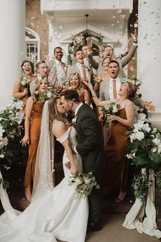 a bride and groom kissing in front of their wedding party