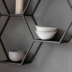 two hexagonal shelves with bowls and candles on them in front of a gray wall