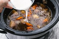 someone pouring milk into a slow cooker filled with food