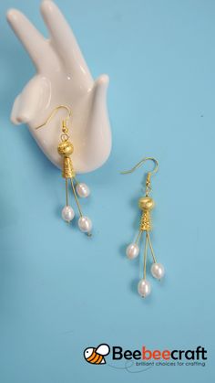 a pair of gold earrings with pearls hanging from it's ear wires on a blue background