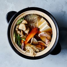 an overhead view of a pot filled with soup and vegetables on a gray table top