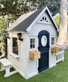 a small white and blue house with a clock on the front door is in the grass