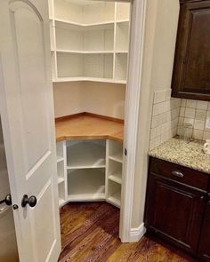 an empty pantry in the corner of a kitchen with wood floors and cabinets on either side