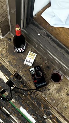 a bottle of wine sitting on the ground next to a window sill with a camera