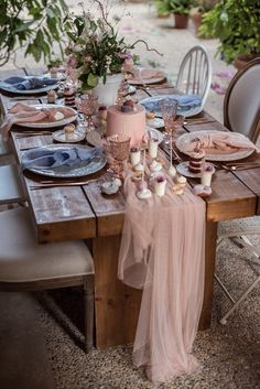 the table is set with pink and blue plates, silverware, candles, and flowers