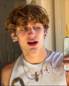 a young man with curly hair is looking at his cell phone while wearing a necklace