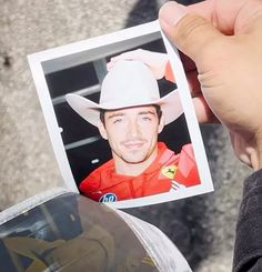 a hand holding up a photo of a man wearing a cowboy hat