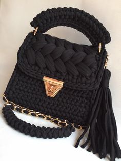 a black handbag with a gold chain and tassels on the handle is sitting on a white surface