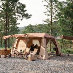 a tent set up in the middle of a forest with two people sitting inside it