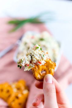 a hand holding up a piece of food with cheese and other toppings in the background