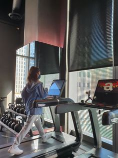 a woman is running on a treadmill with a laptop in her hand and another person behind her