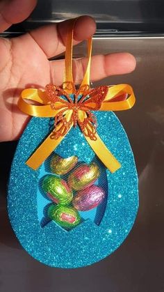 a hand holding an ornament that has been decorated with glitter eggs and a bow