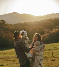 a man and woman are standing in a field with their baby girl, who is wearing a bonnet