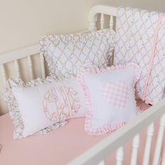 a crib with pink and white bedding and pillows on top of it, next to a teddy bear