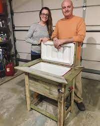 a man and woman standing next to an ice chest in a garage with tools behind them