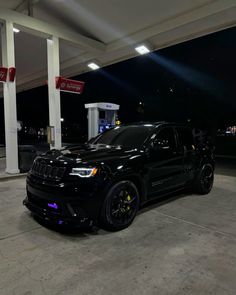 a black jeep parked in front of a gas station at night with its lights on