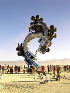 a group of people riding bikes around a giant object in the middle of the desert