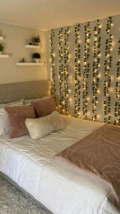 a white bed topped with lots of pillows next to a wall covered in christmas lights