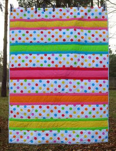 a multicolored polka dot quilt hanging on a clothesline in the grass with leaves around it